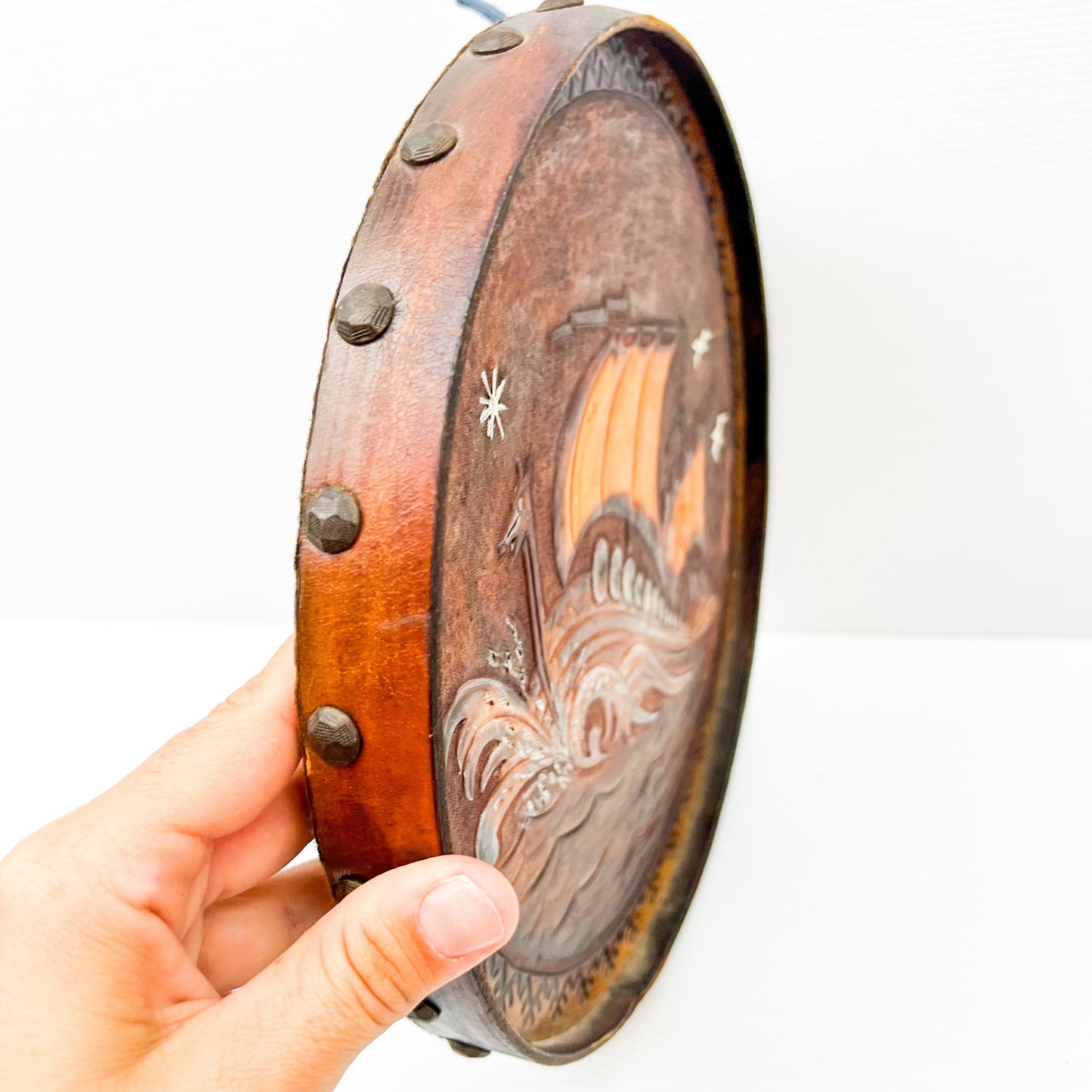 Vintage brown leather round hanging artwork with ship artwork.