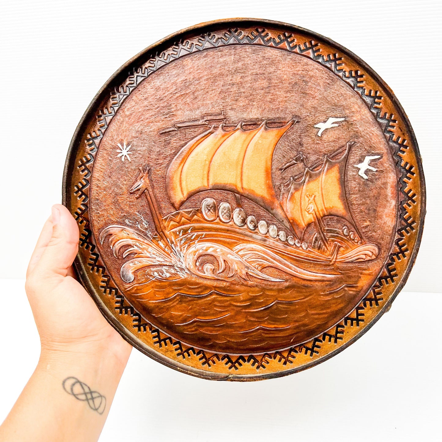 Vintage brown leather round hanging artwork with ship artwork.