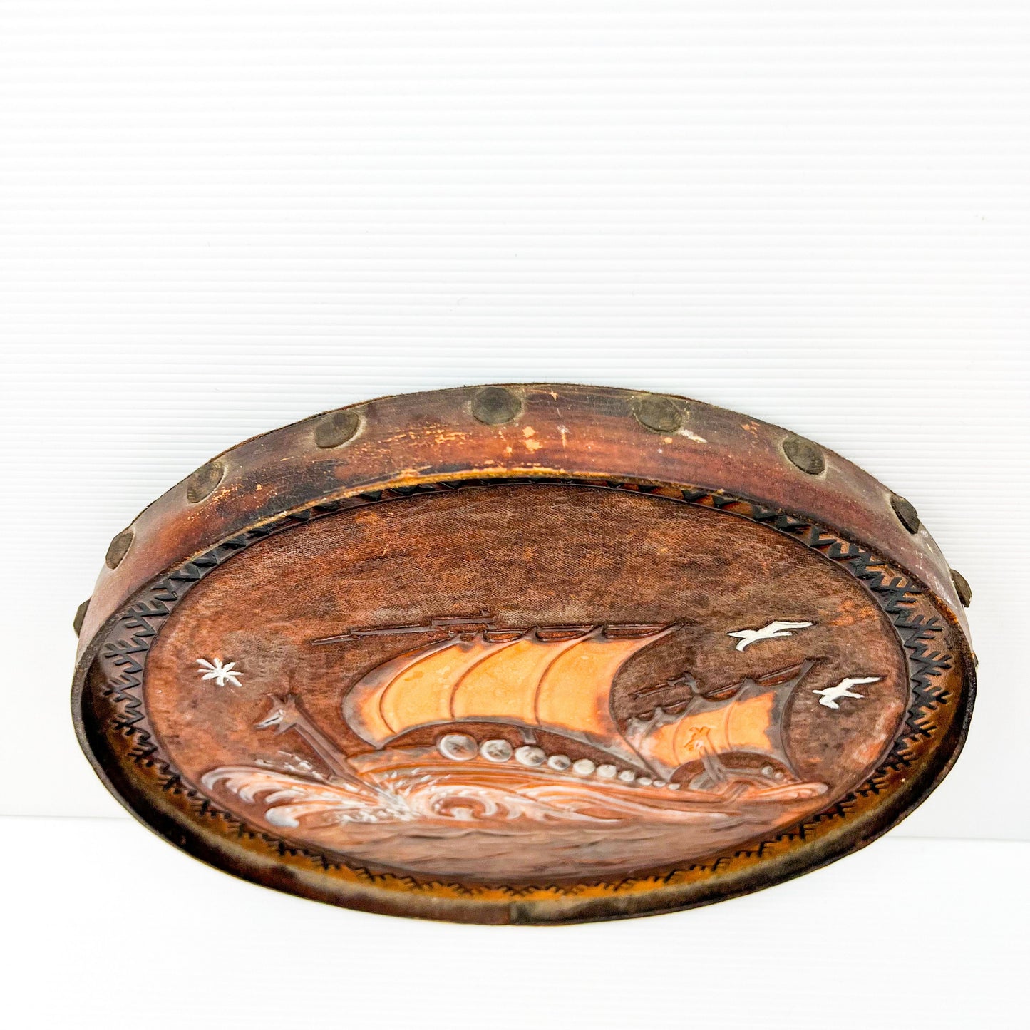Vintage brown leather round hanging artwork with ship artwork.
