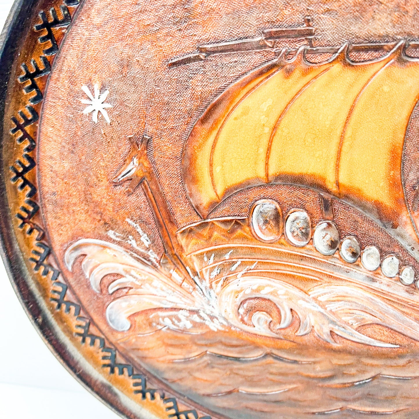 Vintage brown leather round hanging artwork with ship artwork.
