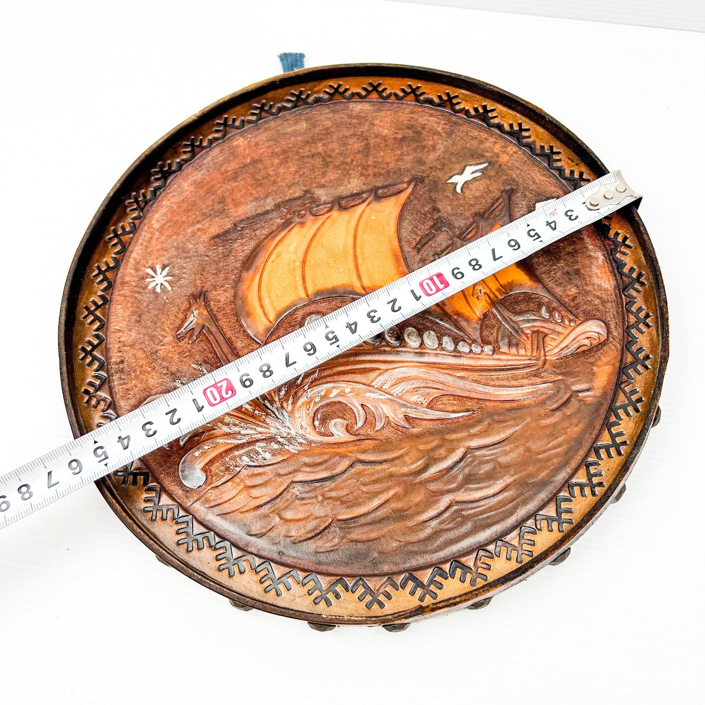 Vintage brown leather round hanging artwork with ship artwork.